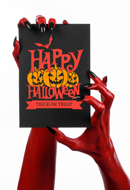 Postcard and Happy Halloween theme: red devil hand with black nails holding a paper card with the words Happy Halloween on a white isolated background in studio - Φωτογραφία, εικόνα