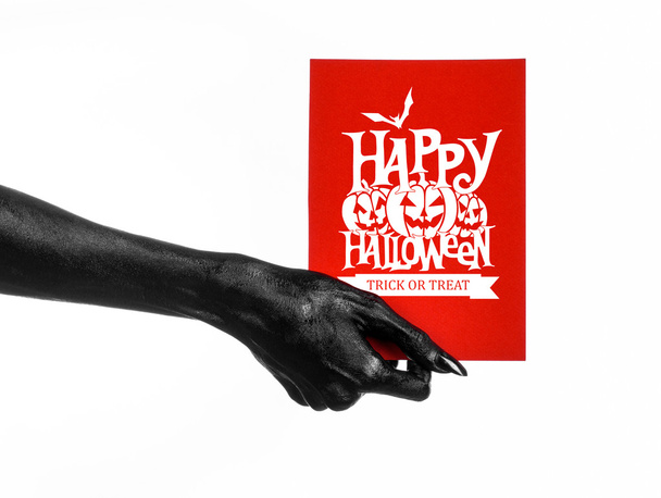 Postcard and Happy Halloween theme: black hand of death holding a paper card with the words Happy Halloween on a white isolated background in studio - Фото, зображення