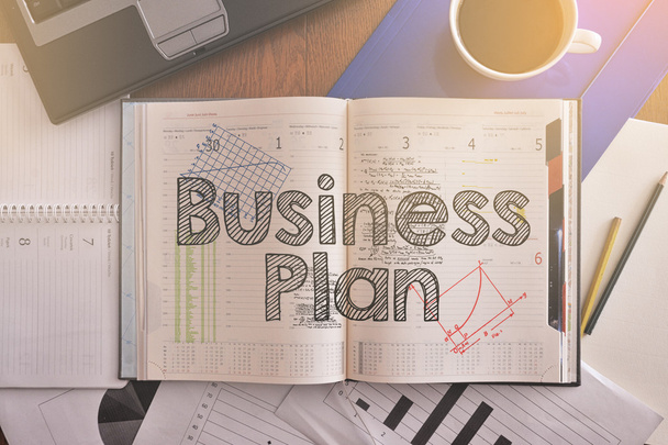 Notebook com texto dentro Business Plan na mesa com café e alguns papéis ao redor
 - Foto, Imagem