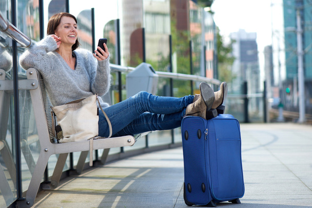 Reisefrau entspannt sich mit Tasche und lächelt aufs Handy - Foto, Bild
