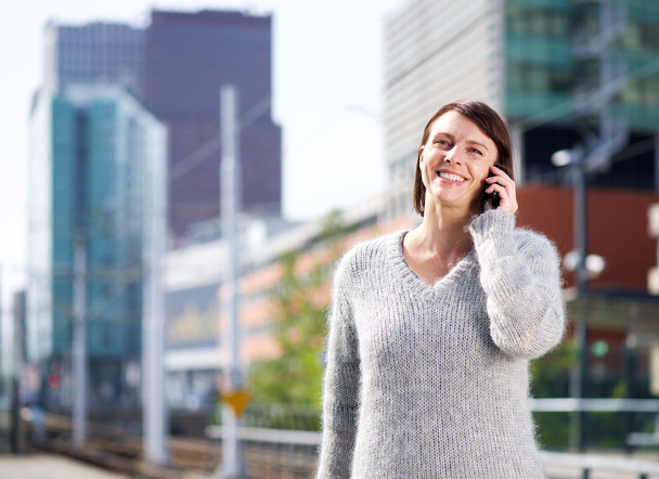 Uśmiechający się kobiety stojącej w mieście z telefonu komórkowego - Zdjęcie, obraz