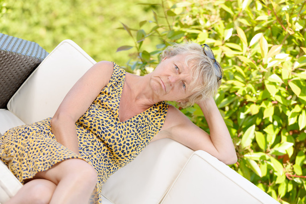 hymyilevä blondi nainen istuu sohvalla, puutarhassa
 - Valokuva, kuva
