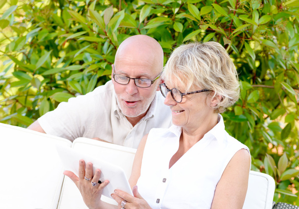middelbare leeftijd couple, glimlachen, met behulp van een tablet in hun tuin - Foto, afbeelding