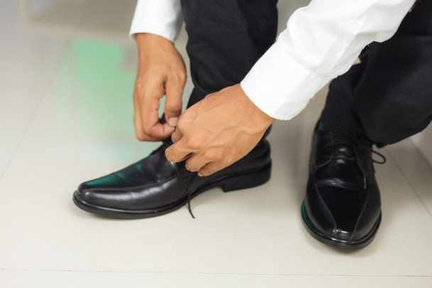 Чоловік зв'язує взуття в приміщенні
 - Фото, зображення