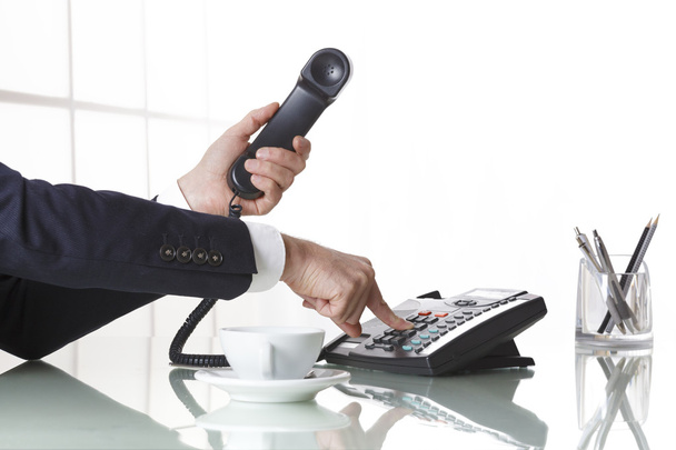 Businessman hands dialing out on a black deskphone - Photo, Image