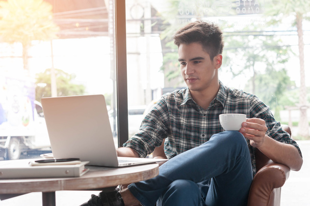 Mann trinkt Kaffee mit Laptop auf Holztisch in Café - Foto, Bild