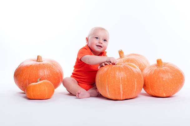 Beautiful baby in orange t-shirt on a white background sits next - Foto, Imagen