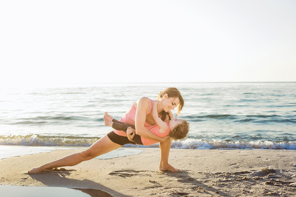 Rodzina treningu - matka i córka robi ćwiczenia na plaży. - Zdjęcie, obraz