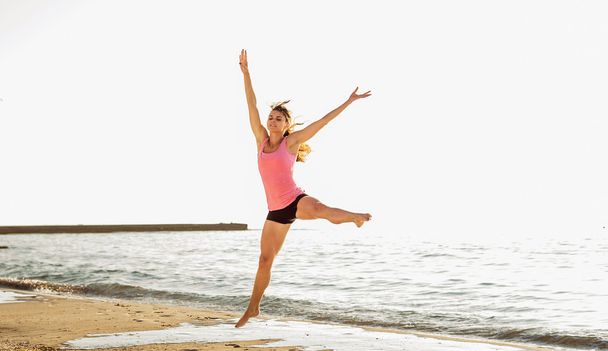beautiful sporty woman jumping on seaside, gymnast female doing - Photo, Image