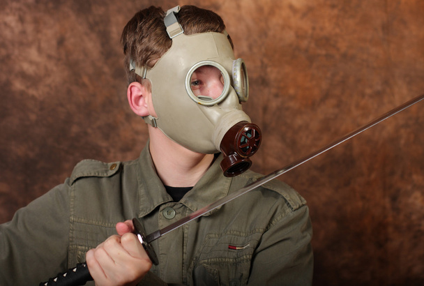 防毒マスクと茶色のバティックの背景に刀を持つ男 - 写真・画像