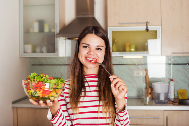Nuori valkoihoinen nainen syö salaattia keittiössä. Terveet orgaaniset
 - Valokuva, kuva