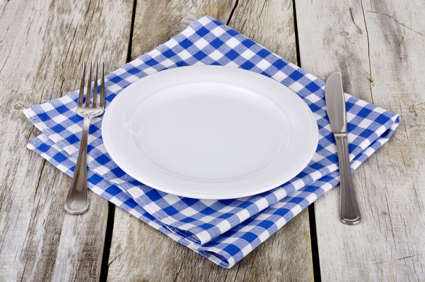 Lege plaat met mes en vork op blauw-wit geruite tafellaken op houten tafel. - Foto, afbeelding