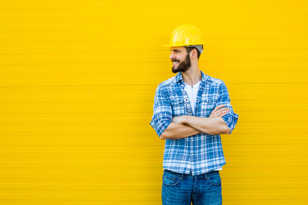 adult worker with helmet on yellow wall - Foto, Imagen