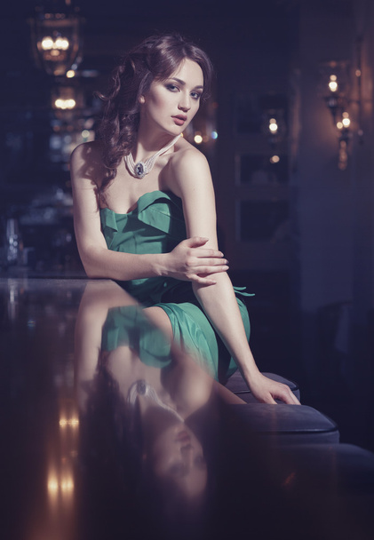 elegantes Mädchen in grünem Kleid sitzt an der Bar - Foto, Bild