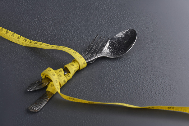 Lowlight sleutel van lepel, vork en geel meetlint met waterdruppel op grijze achtergrond - Foto, afbeelding