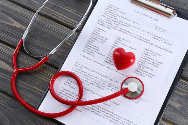 red rubber stethoscope with plastic heart and medical history on wooden background - 写真・画像