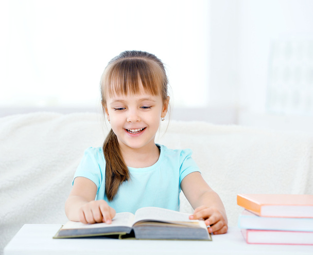 Beautiful little girl sitting on sofa with book, on home interior background - Photo, Image