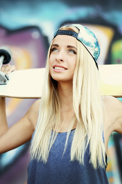 Young woman with skating board  on painted wall background - Foto, Imagem