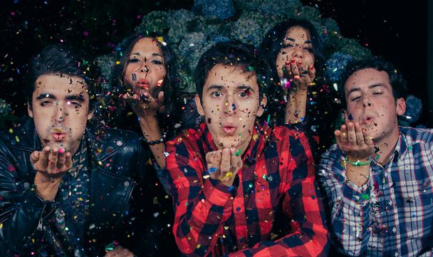 Friends group blowing confetti to the camera in a party - 写真・画像