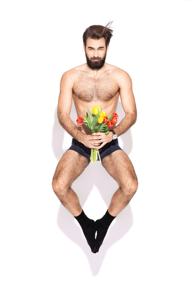 Young man with a beard and flowers jumping in the studio - Φωτογραφία, εικόνα
