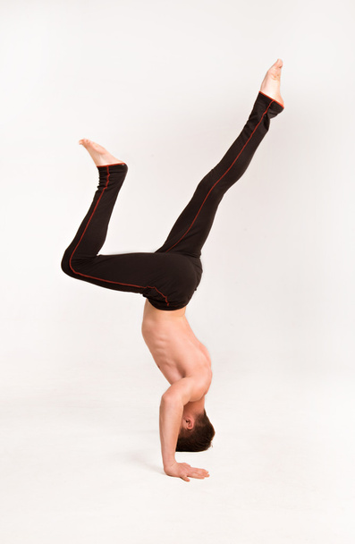 λεπτός άνθρωπος κάνει γυμναστικές ασκήσεις. Γυμναστής στέκεται στα χέρια - Φωτογραφία, εικόνα