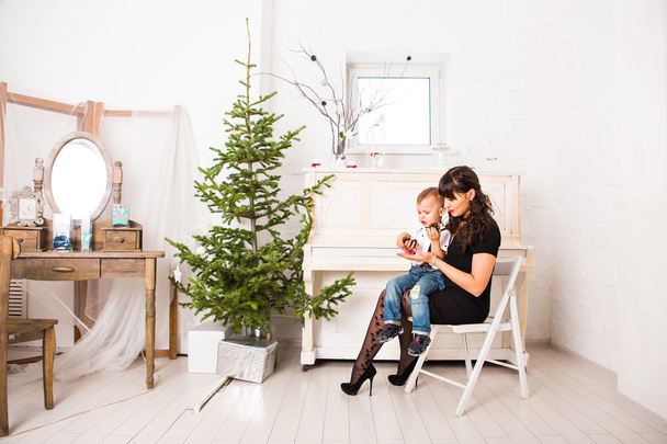 mãe e seu filho brincando perto de um abeto decorado para o Natal
 - Foto, Imagem