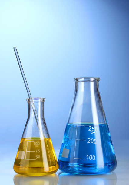 Two flasks with yellow and blue liquid with reflection on blue background - Photo, Image
