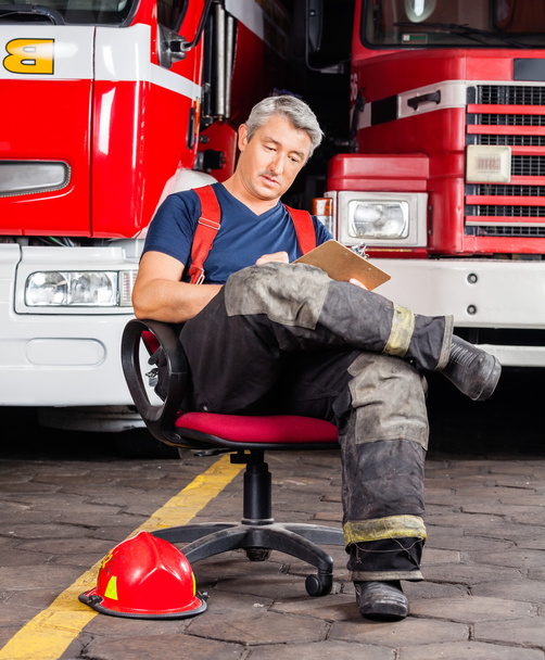 Fireman Writing On Clipboard While Sitting Against Trucks - Φωτογραφία, εικόνα