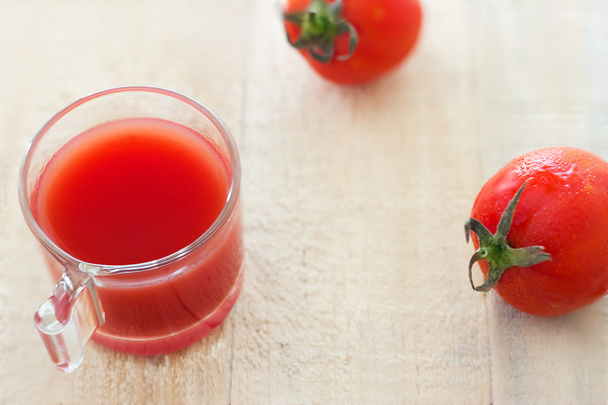 Свежий томатный сок в траве и несколько помидоров на бледном деревянном фоне
 - Фото, изображение