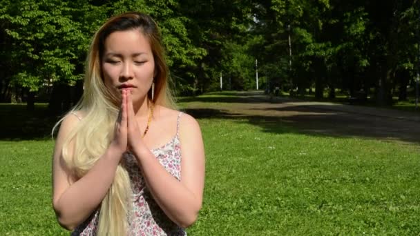 młoda atrakcyjna azjatycka kobieta modli się w parku - zbliżenie - Materiał filmowy, wideo