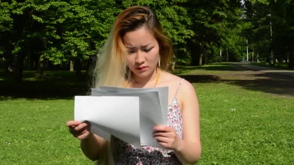 young attractive asian woman searches in pages something in the park - close up - Video