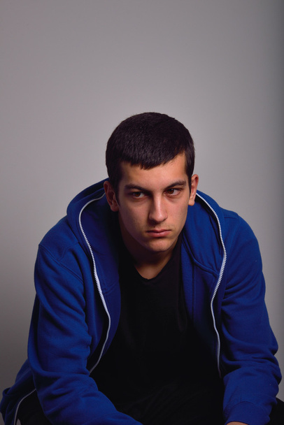 Sad teenager with blue sweatshirt standing against a dirty wall - Photo, image