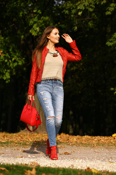 Young woman in fashion red jacket and red bag walking in autumn - Foto, Bild