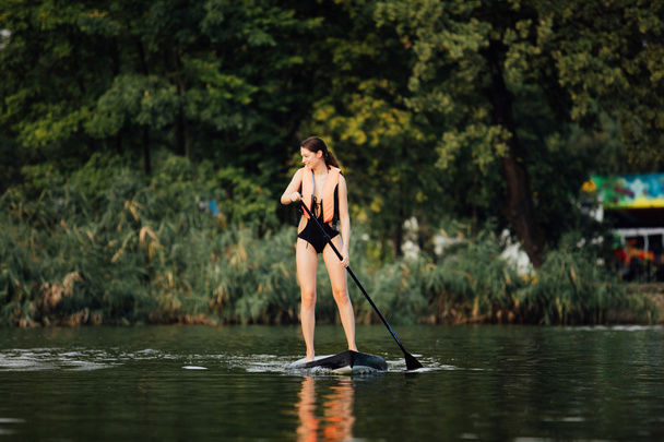 woman doing stand up paddle on a lake surrounded by trees - Foto, afbeelding