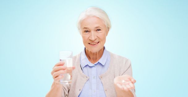 happy senior woman with water and medicine - 写真・画像