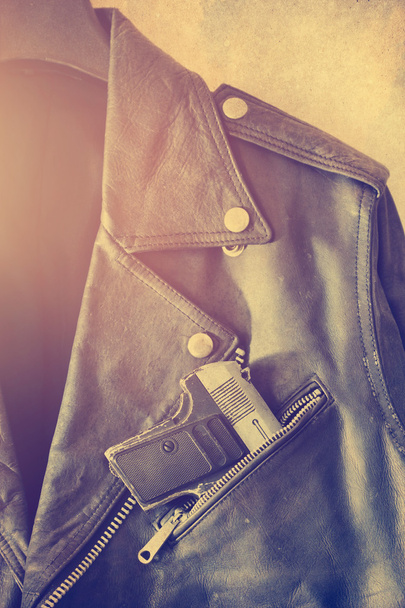 Vintage old  leather jacket with gun in the pocket on grain paper background - Photo, Image