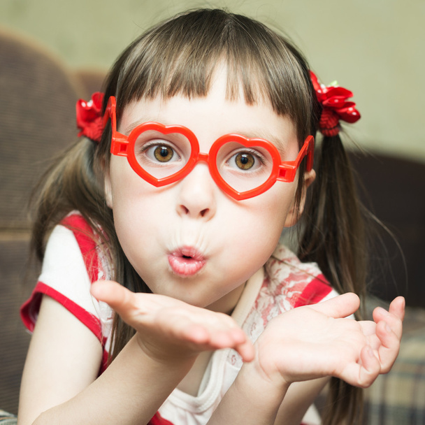 Cute little girl with glasses in the shape of a heart sends an air kiss - Fotografie, Obrázek