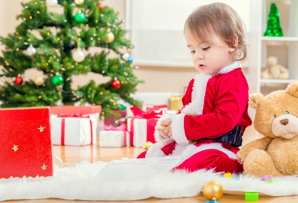 girl in a santa suit playing by the Christmas tree - Foto, afbeelding