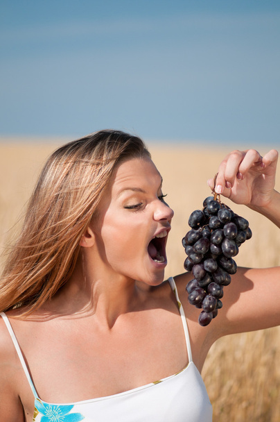 Woman in wheat field eating grapes. Summer picnic. - Photo, Image