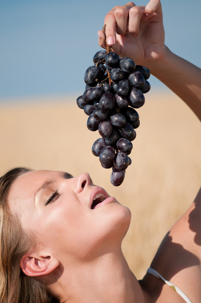 Woman in wheat field eating grapes. Summer picnic. - Φωτογραφία, εικόνα