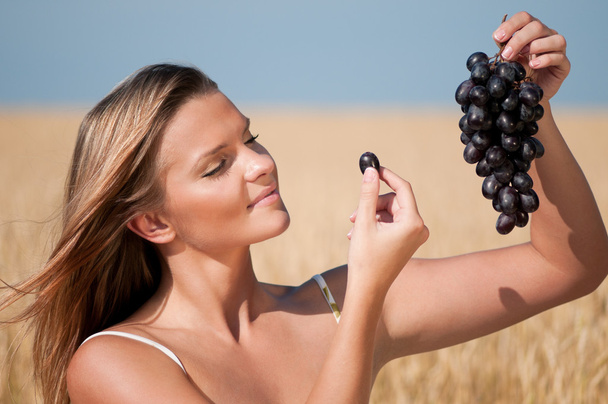 Woman in wheat field eating grapes. Summer picnic. - Фото, зображення