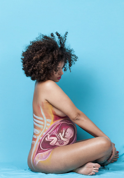 Pregnant woman crossed legged sitting with baby painted on belly - Foto, immagini