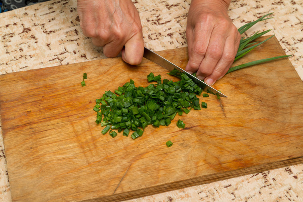 Шеф рубає зелену цибулю ножем на обробній дошці
 - Фото, зображення