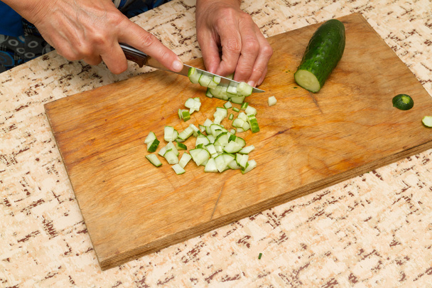 De chef-kok snijdt de komkommer op een houten bord. - Foto, afbeelding