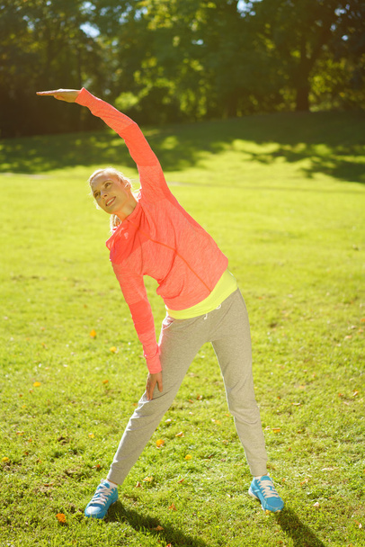 Здоровая женщина, занимающаяся растяжкой тела в парке
 - Фото, изображение
