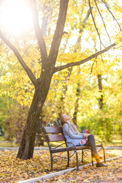 girl sitting on the bench in autumn park - Fotó, kép