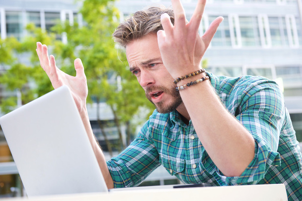 Stressed man looking at laptop with hands raised - Photo, Image