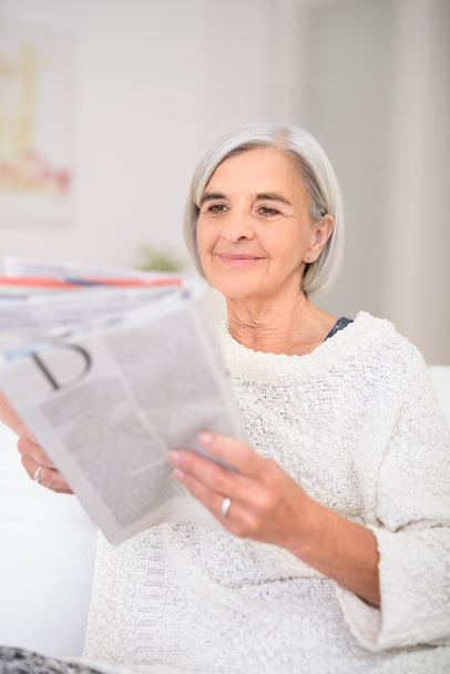 年配の女性は、リビング ルームで雑誌を読む - 写真・画像