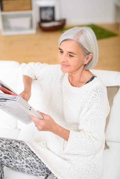 Μέσης ηλικίας γυναίκα ανάγνωση περιοδικό στο καναπέ - Φωτογραφία, εικόνα