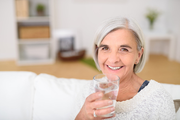 Senior Woman at the Couch Holding Glass of Water - Foto, imagen